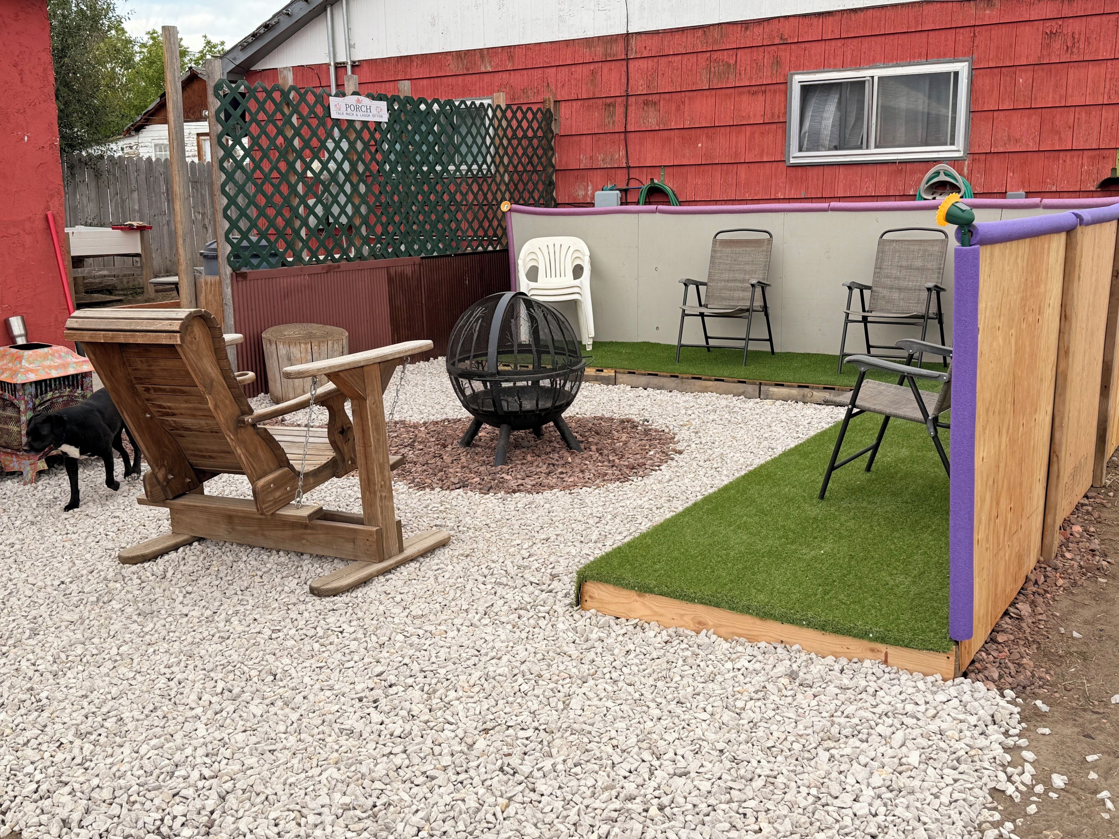 Een achtertuin met een houten speeltuintje, een vuurkorf en tuinmeubilair.