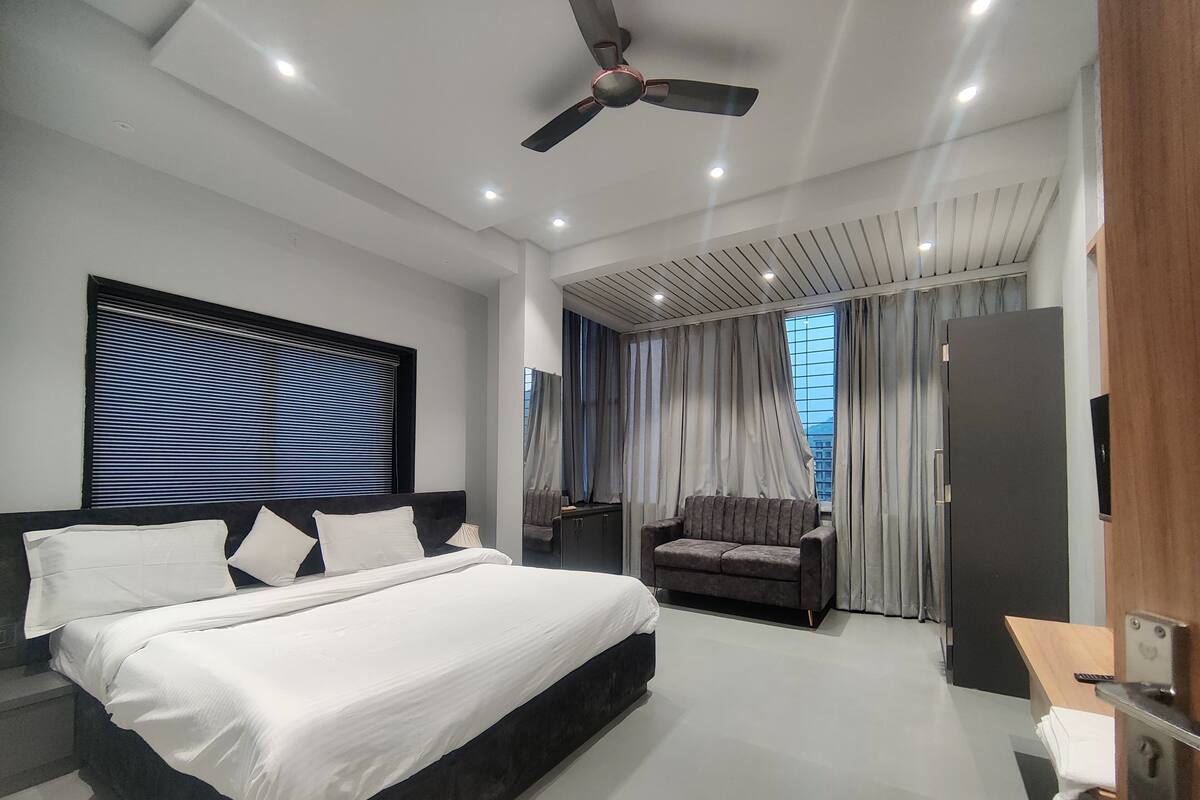 Una habitación de hotel moderna con una cama grande, un sofá, un ventilador de techo y vistas a la ciudad desde la ventana.