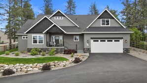 A two-story house with a grey exterior, a front porch with a seating area, a garage, and a driveway. - Four Bedroom Retreat Near Hayden Lake: Game Room, Family Fun (Coeur d'Alene)