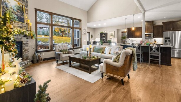 A spacious living room with a fireplace, large windows, and a kitchen area with dark wooden cabinets and stainless steel appliances. - Four Bedroom Retreat Near Hayden Lake: Game Room, Family Fun (Coeur d'Alene)