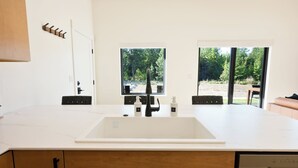 Une cuisine moderne dotée d’un grand évier blanc, de meubles en bois et offrant une vue sur l’extérieur grâce à de grandes fenêtres.