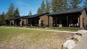 Une rangée de cabanes dotées d’espaces extérieurs aménagés, entourées d’arbres.