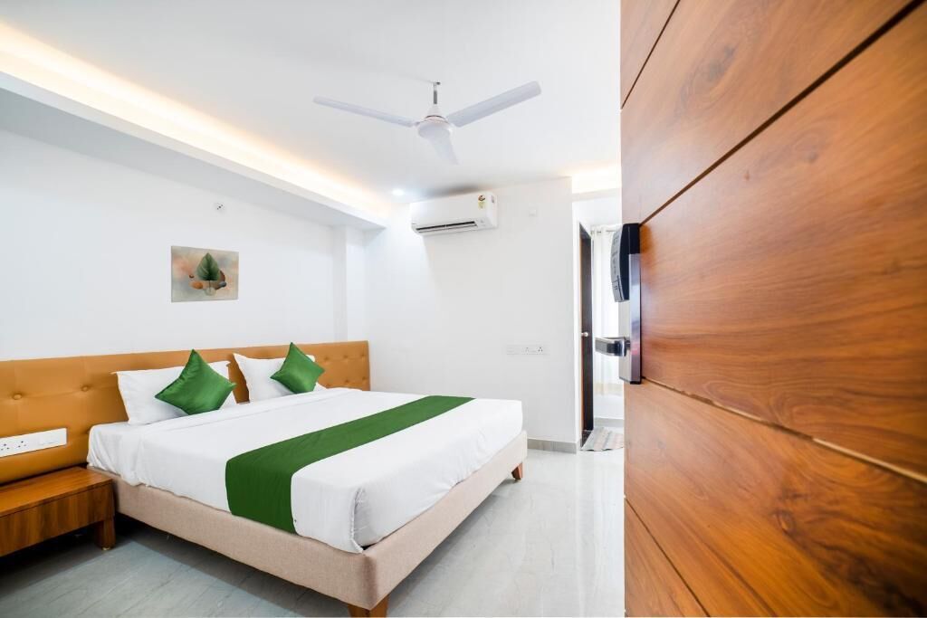 Habitación de hotel con cama, ventilador de techo, unidad de aire acondicionado, armario de madera y una mesita de noche.