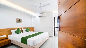 Habitación de hotel con cama, ventilador de techo, unidad de aire acondicionado, armario de madera y una mesita de noche.