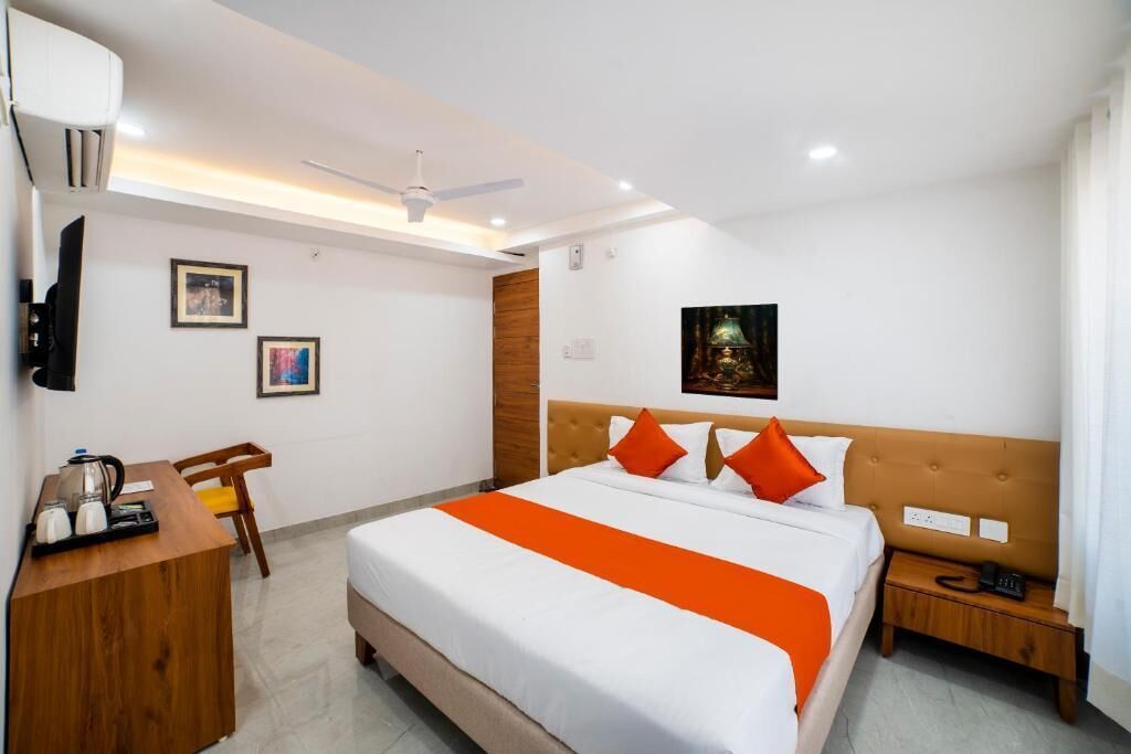 A hotel room with a bed, a desk, a chair, a nightstand, a wall-mounted TV, and a ceiling fan.