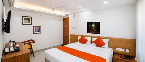 A hotel room with a bed, a desk, a chair, a nightstand, a wall-mounted TV, and a ceiling fan.