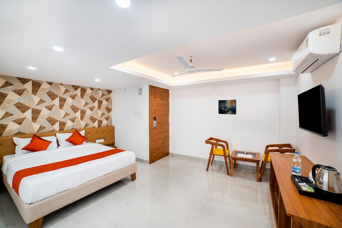 Quarto de hotel com cama, escrivaninha, cadeiras, televisão e ar condicionado.