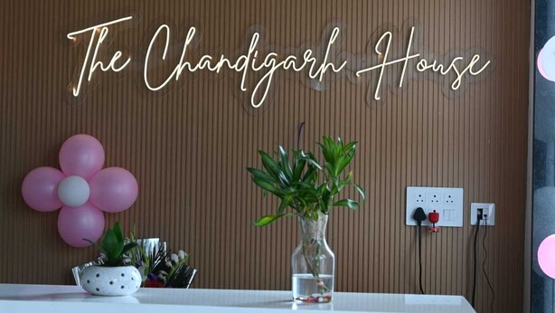 A reception area with a sign reading "The Chandigarh House," a potted plant, a vase with flowers, and a wall socket. - The Byke Business - Chandigarh House (Bhopal)