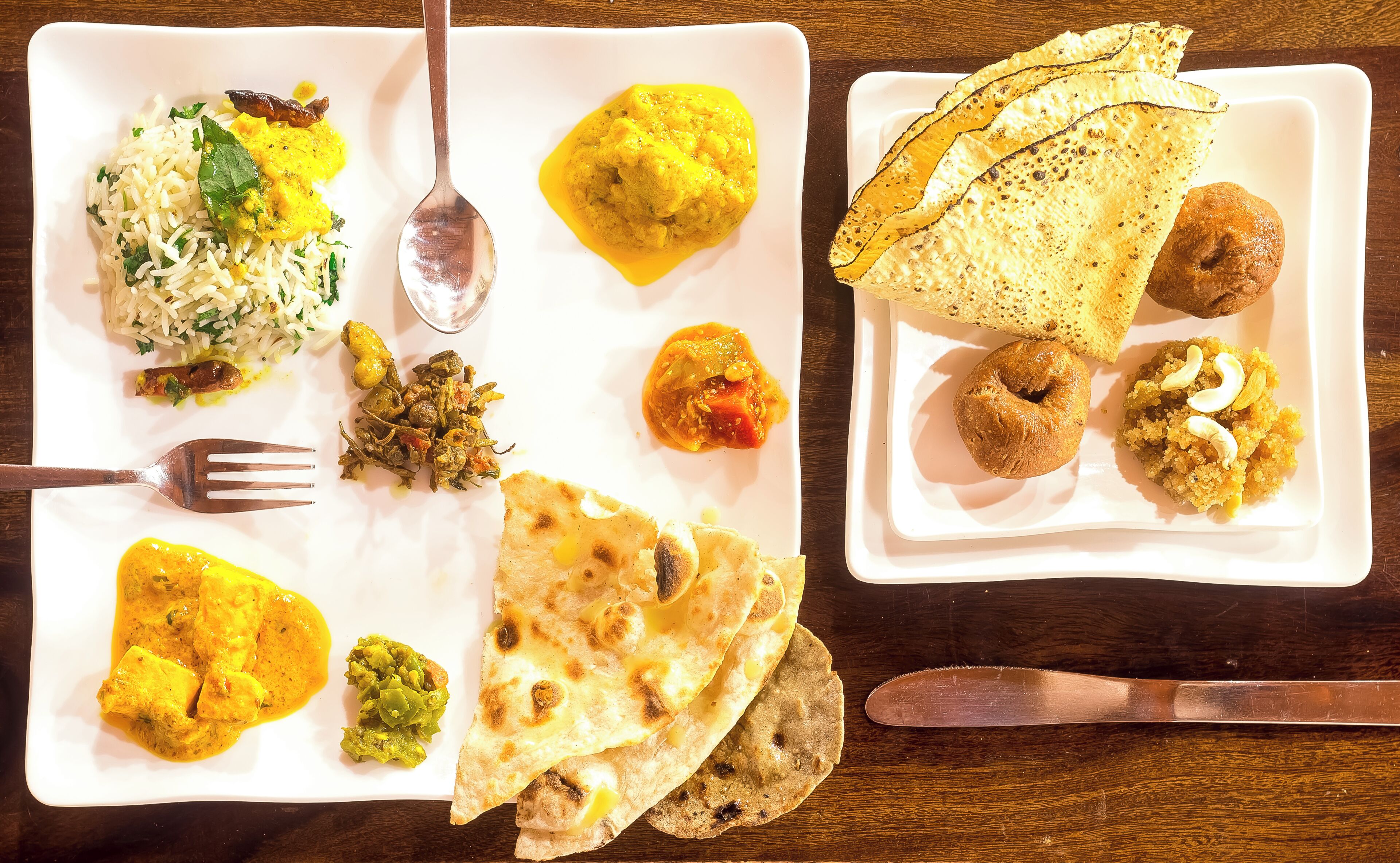 Une assiette blanche contenant divers plats indiens, notamment du riz, un curry et des galettes.