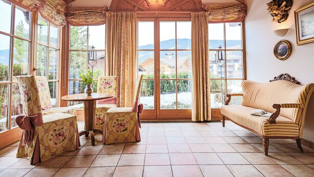 Ein gemütliches Zimmer mit Holzbalkendecke, großen Fenstern, einem Tisch mit Stühlen und einer Couch.