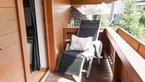 Ein Holzbalkon mit einem Korbstuhl, einem kleinen Tisch mit Flasche und Gläsern sowie Blick ins Grüne.