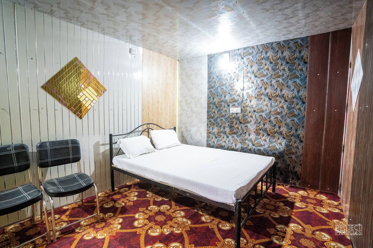 A room with a bed, a patterned carpet, a wall with a geometric design, and a wooden door.