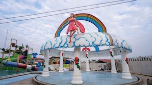 Une fontaine d’eau surmontée d’une statue de femme, entourée d’un belvédère blanc doté de colonnes et d’une arche en forme d’arc-en-ciel.