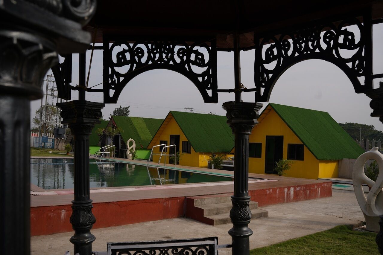 A pool area with a green-roofed building, a clear sky, and a decorative metal archway.