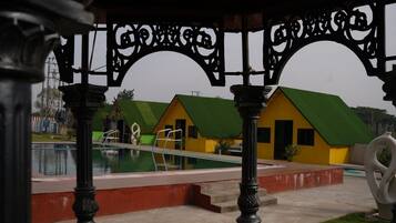 A pool area with a green-roofed building, a clear sky, and a decorative metal archway.
