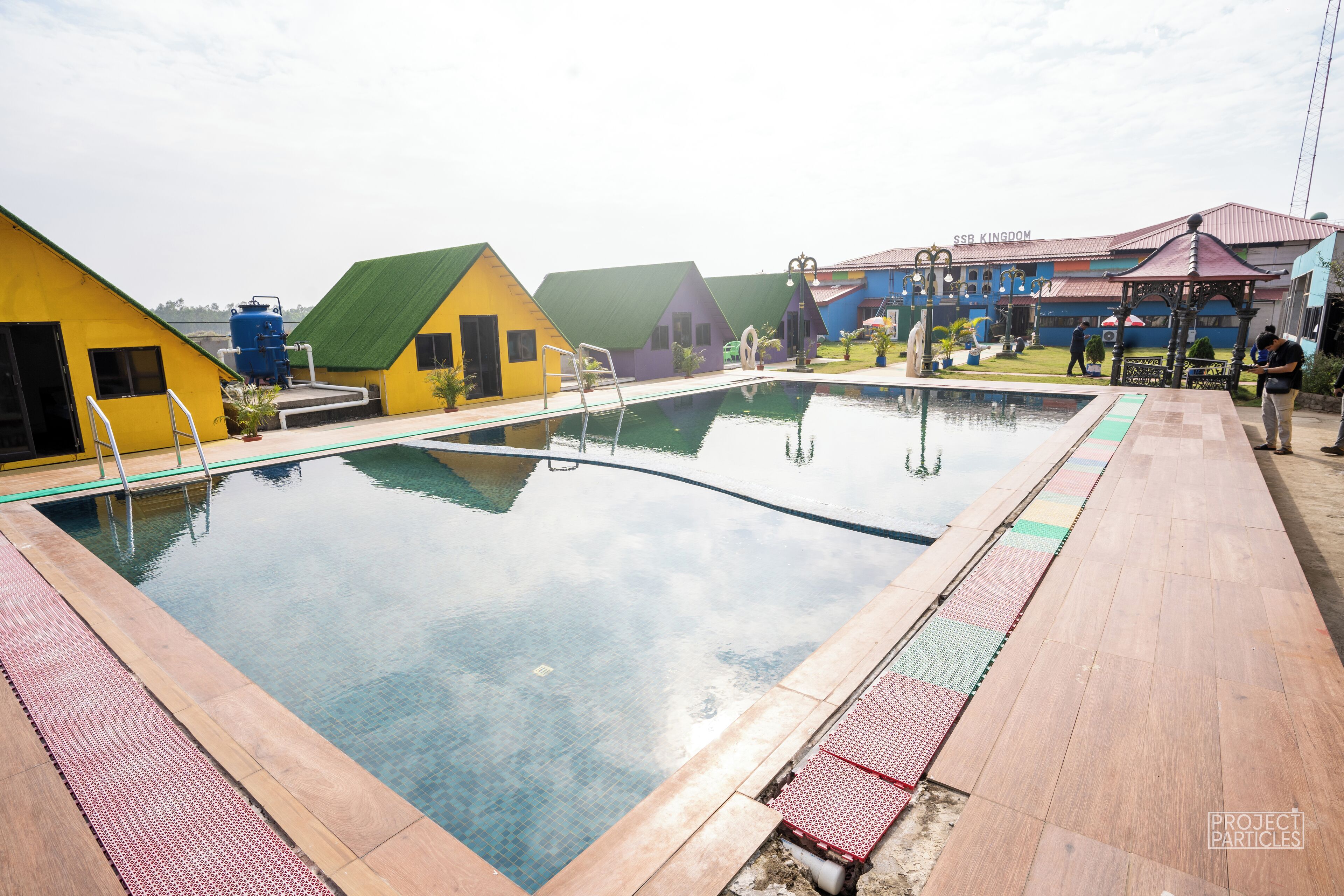 A swimming pool with a wooden deck and colorful buildings in the background.