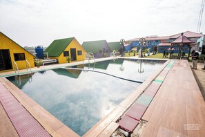 Ein Schwimmbecken mit Holzterrasse und farbenfrohen Gebäuden im Hintergrund.