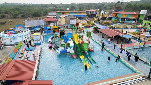 Un parc aquatique doté de nombreux toboggans et de plusieurs piscines, entouré de bâtiments aux couleurs vives et d’un paysage vallonné.