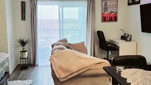 A cozy bedroom with a bed, a desk, and a chair. There is a window with curtains, a plant, and a wall with a picture. - Cozy Condo-Apartment/Suite in Brampton (Brampton)