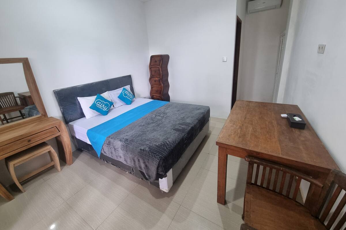 A bedroom with a bed, a wooden nightstand, a wooden table, and a mirror.