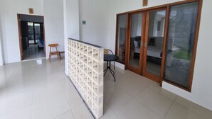 A spacious room with a sliding glass door leading to a balcony, a small seating area with a chair, and a tiled floor. - Mulia Cottage Jimbaran (Jimbaran)
