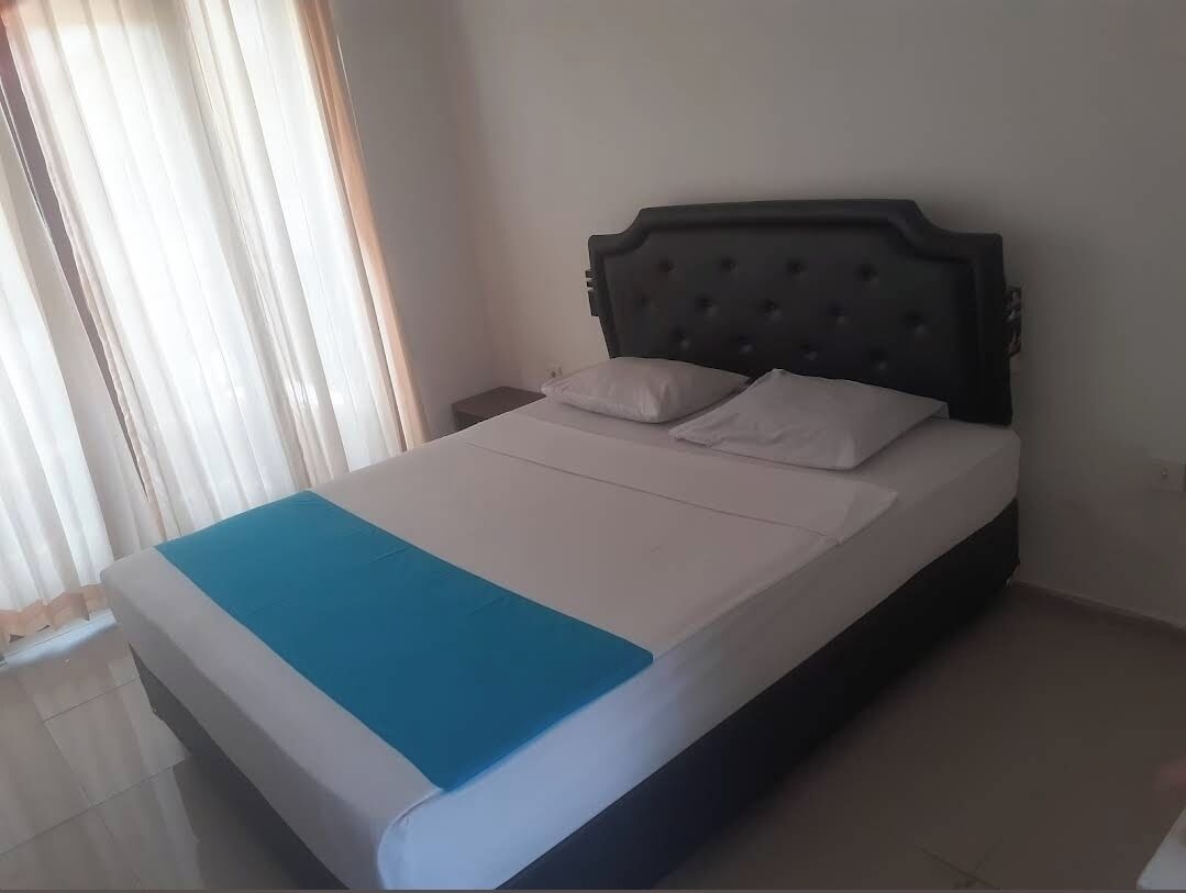 A single bed with a dark headboard, white bedding, and a blue accent at the foot.