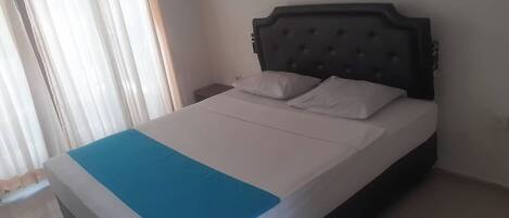 A single bed with a dark headboard, white bedding, and a blue accent at the foot.