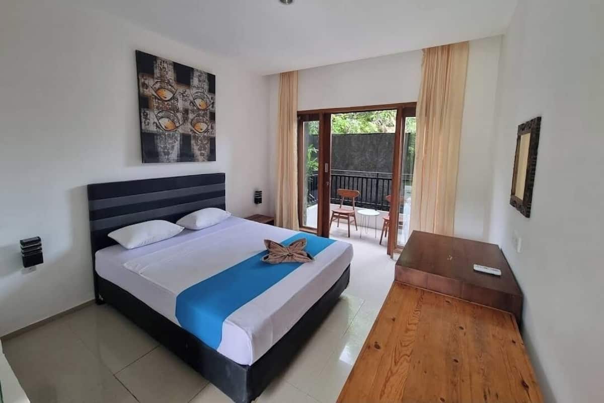 A bedroom with a large bed, a painting on the wall, and a balcony with a table and chairs.