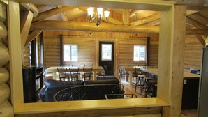 Interior de una cabaña de troncos con comedor, chimenea y cocina.