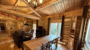 Interior de una cabaña de madera con una mesa de comedor, sillas, un sofá y una chimenea.