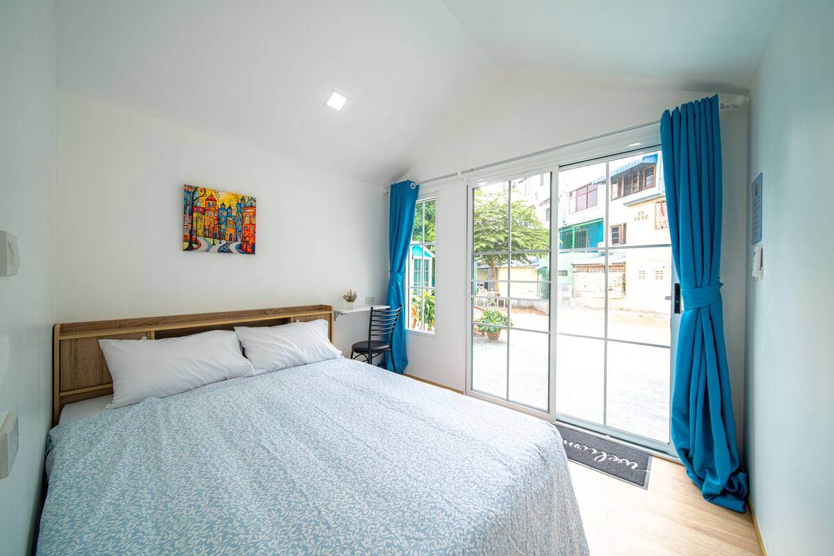 Una camera da letto con un letto, una sedia, una finestra con tende e una porta che dà su uno spazio all'aperto.