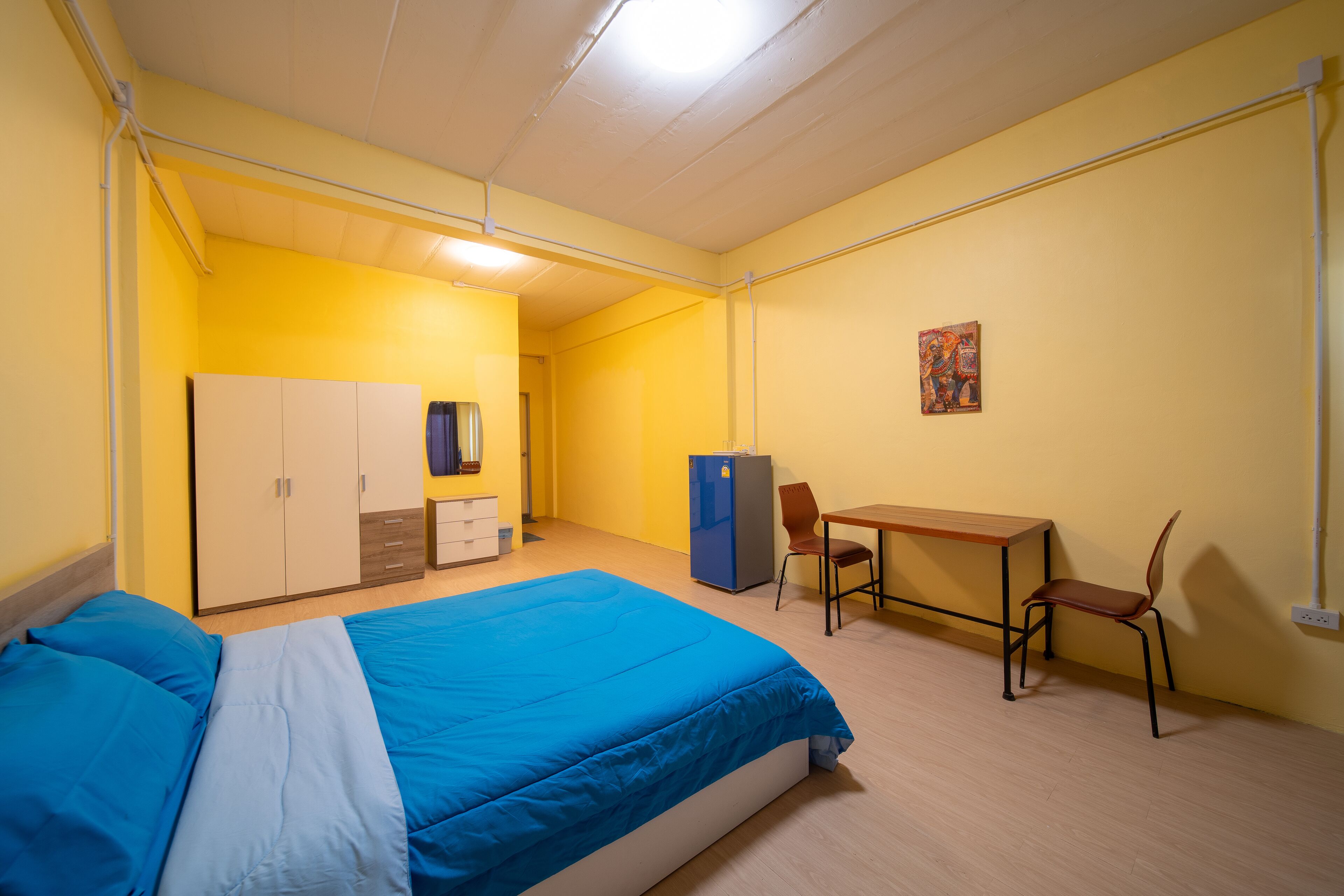 A room with a bed, a desk, a chair, a wardrobe, and a painting on the wall.