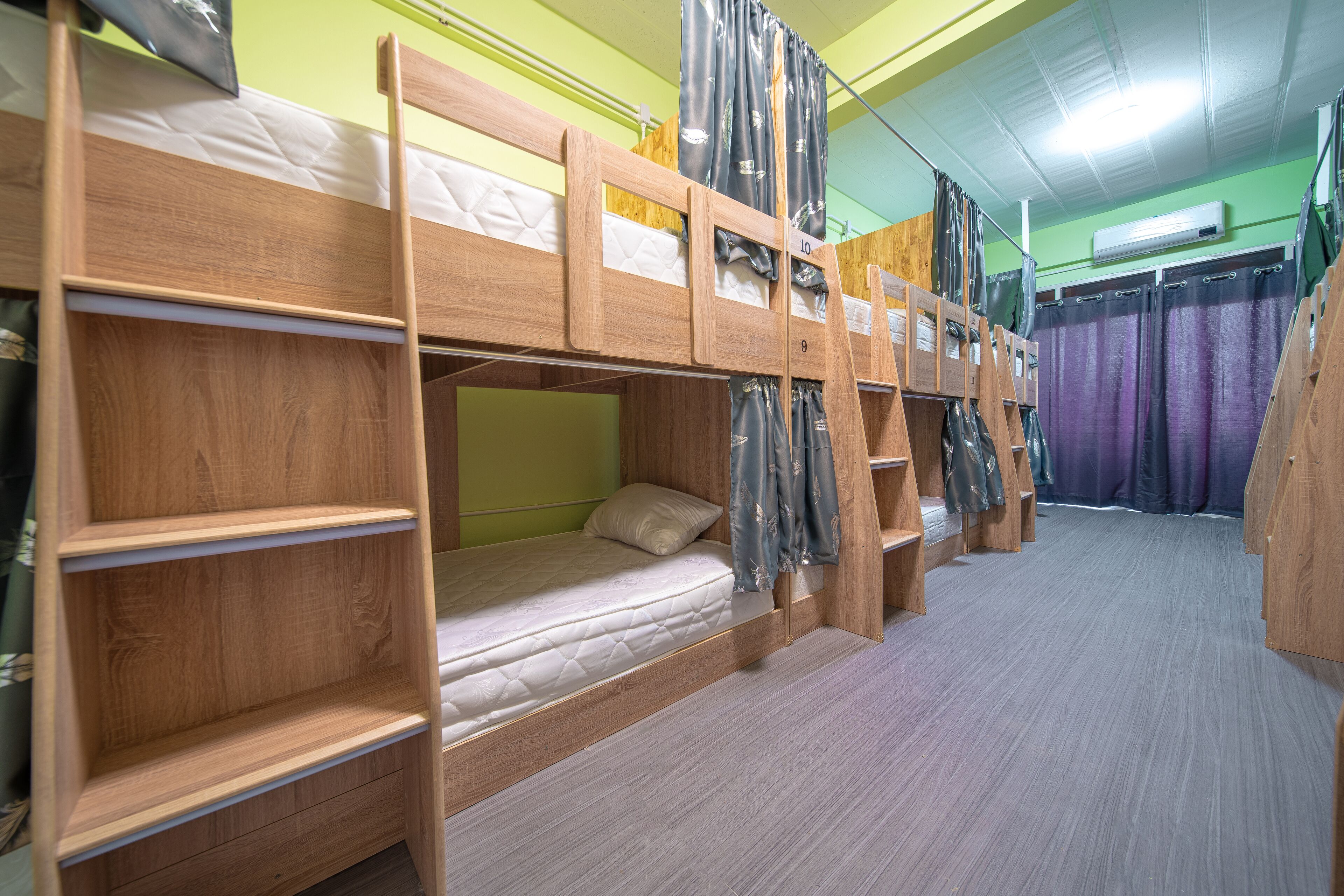 A bunk bed room with a green wall, a window with curtains, and a wooden floor.