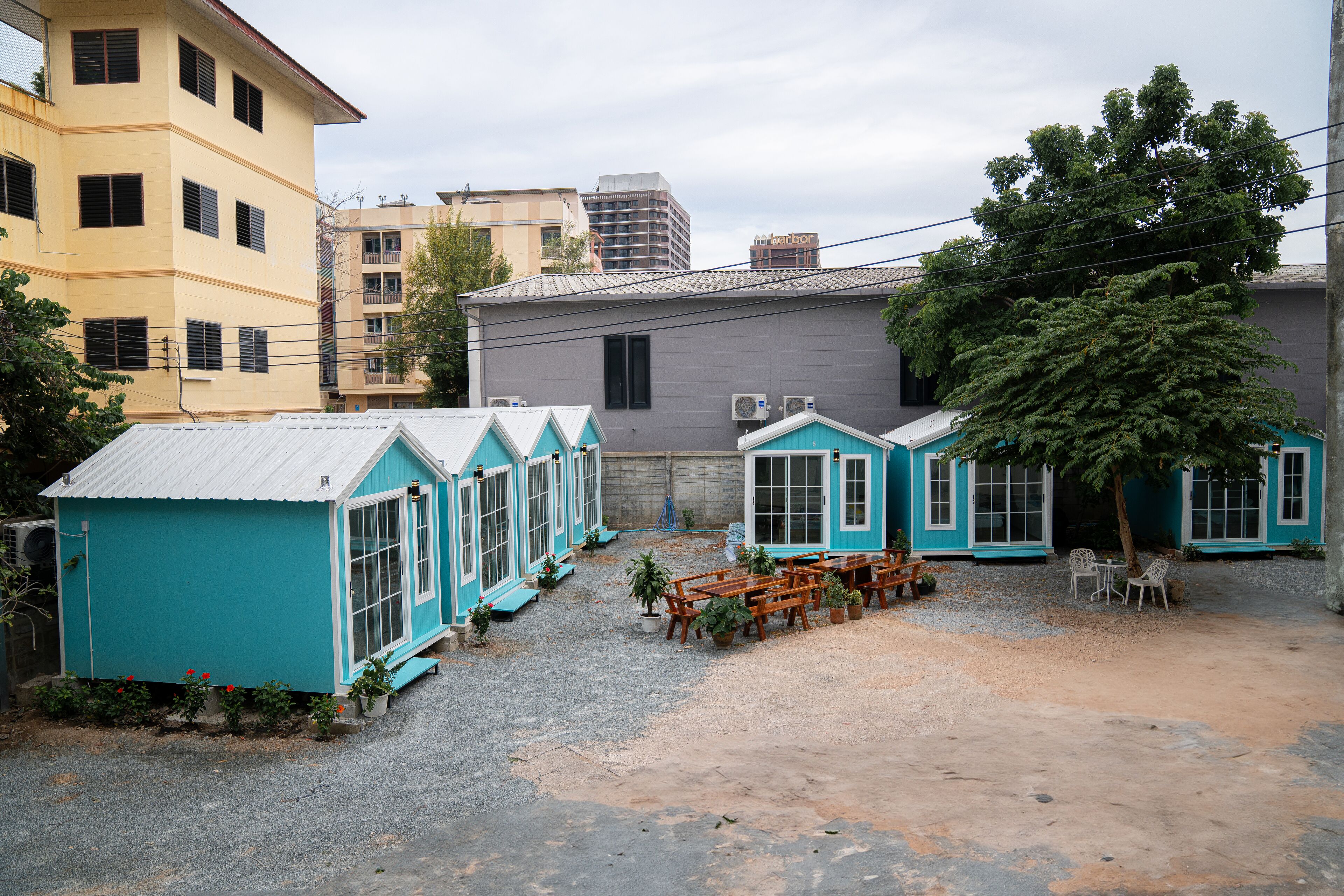 Un patio con varios edificios pequeños azules, mobiliario exterior y un árbol grande.