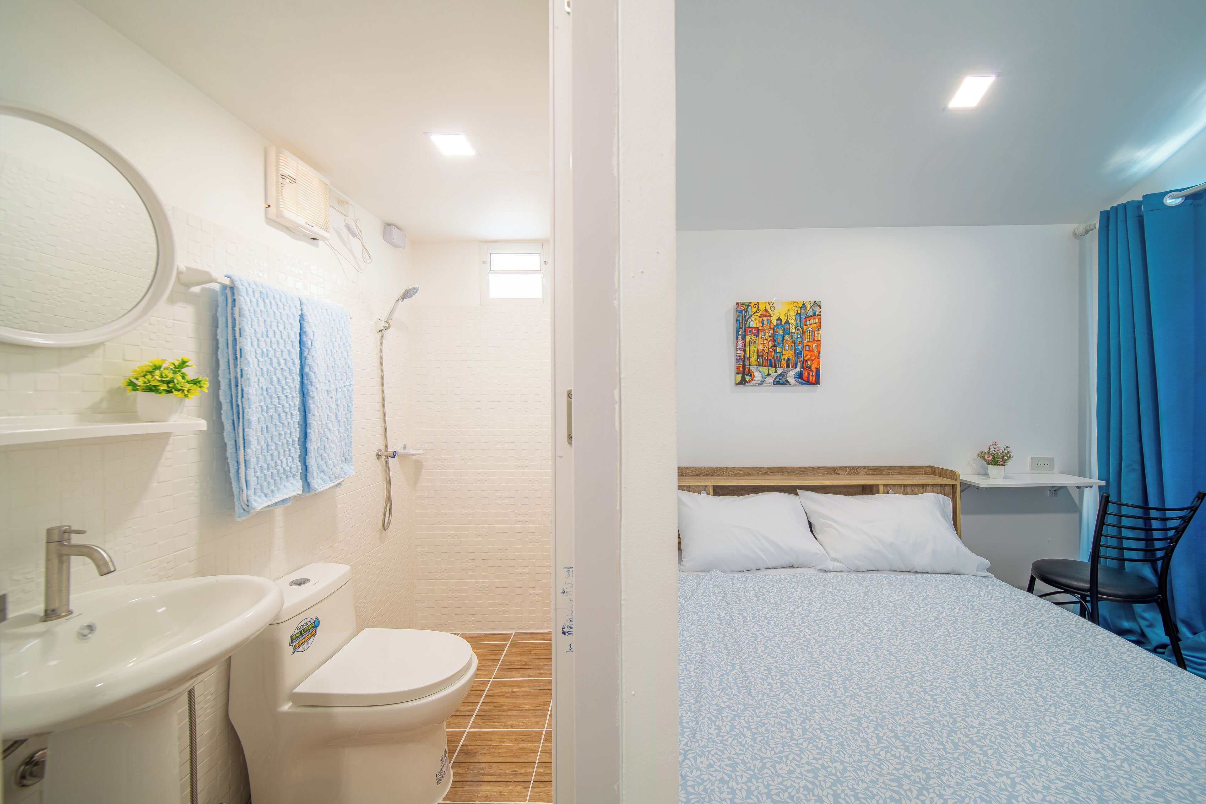 Een badkamer met een wastafel, toilet en douche, en een slaapkamer met een bed, stoel en kunst aan de muur.