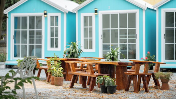 A row of blue and white cottages with wooden tables and chairs, surrounded by potted plants. - UrbanNest Hostel  (Pattaya)