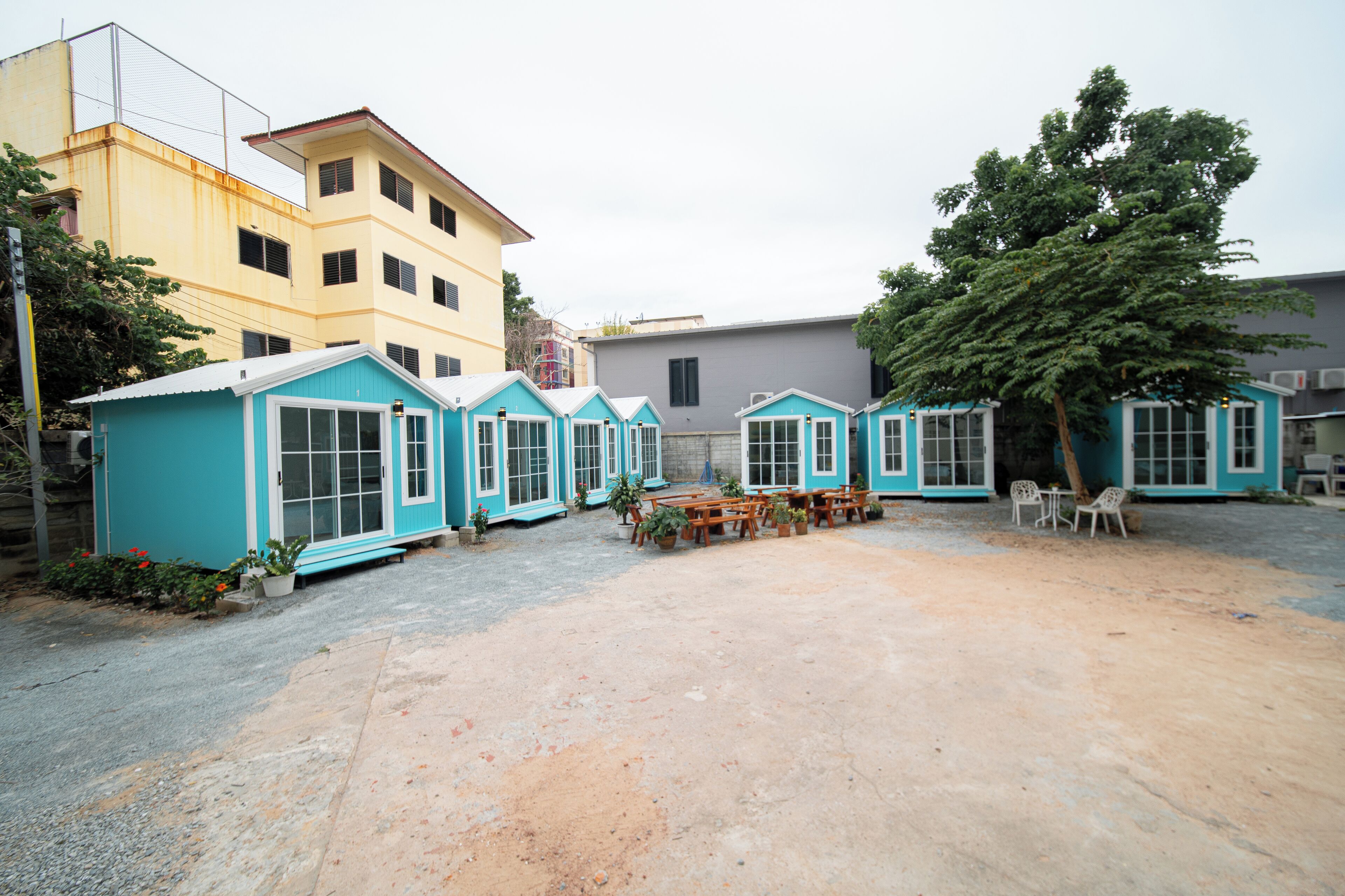 Un patio con varias cabañas azules pequeñas, un árbol grande y un edificio al fondo.