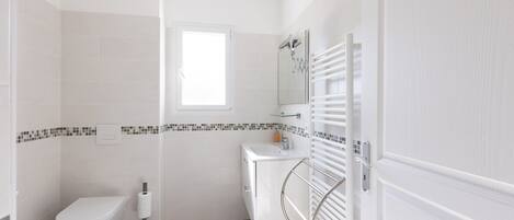 Et badeværelse med toilet, håndvask, spejl og håndklædestang.