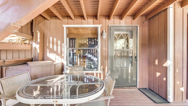 A covered patio with a glass table and chairs, wooden walls, and a door with a glass panel. - Walk to Angel Fire Resort: Condo w/ Furnished Deck (Angel Fire)