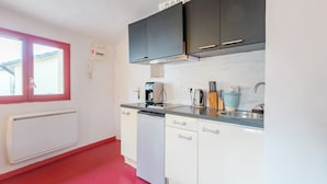 Una cocina compacta con armarios blancos, lavavajillas, cafetera y fregadero.