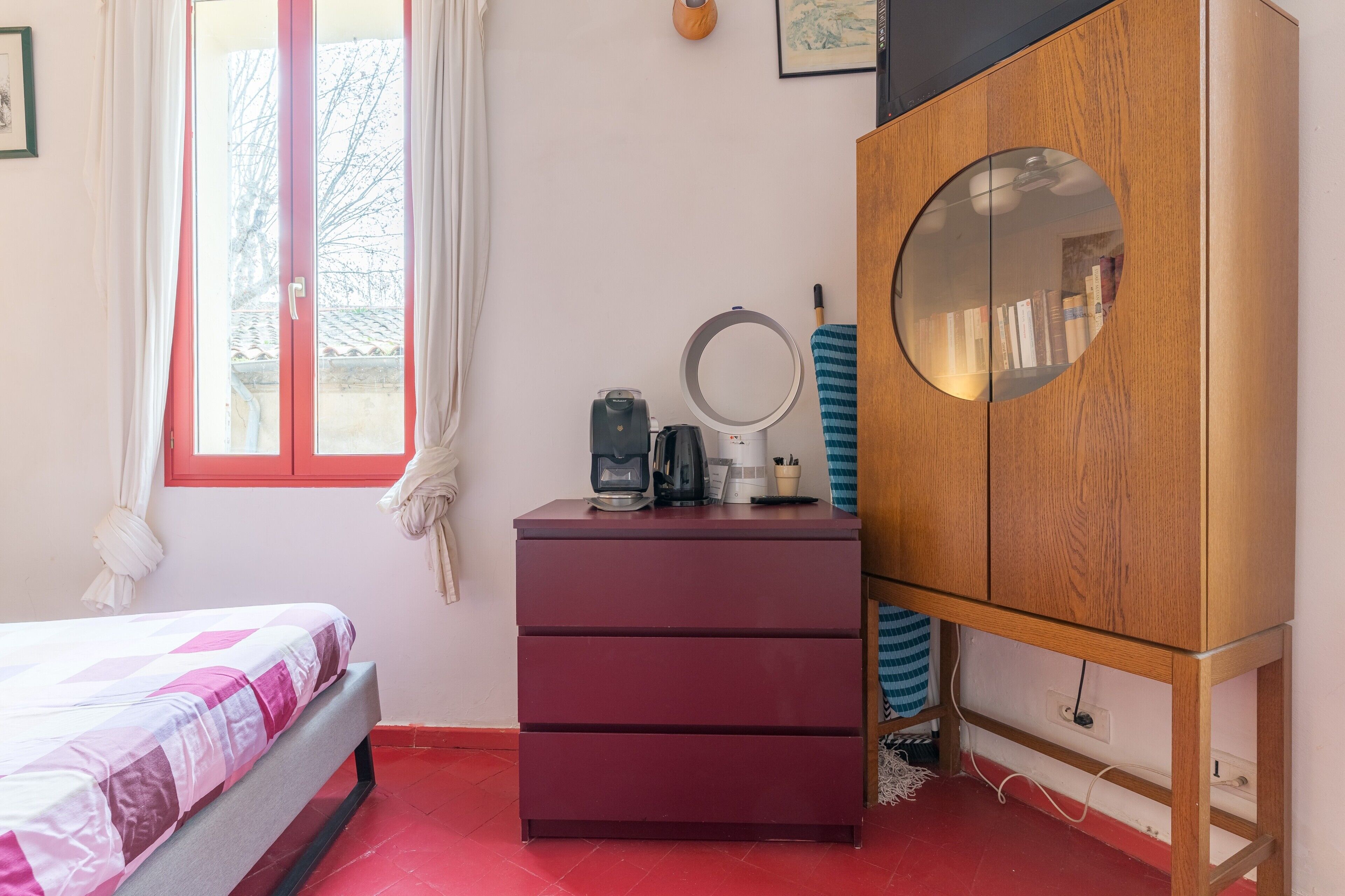 Une chambre à coucher avec un lit, une commode, un miroir et une fenêtre avec des rideaux.