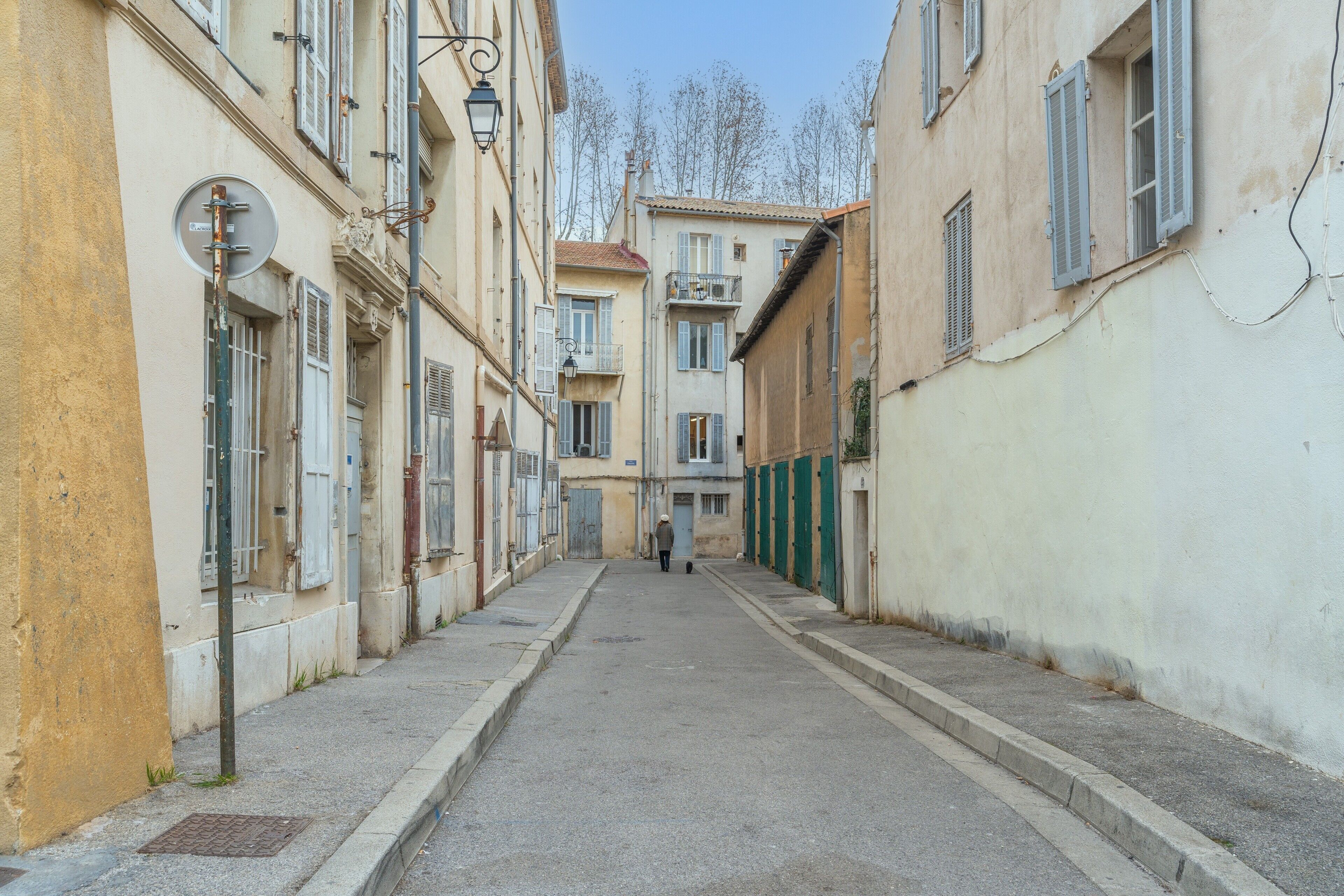 A narrow street with buildings on either side, a person walking down the street, and a clear sky.