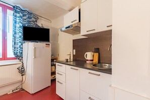 Een praktische keuken met witte kastjes, een roestvrijstalen spoelbak, een inbouwoven en een raam met een gestreept gordijn.