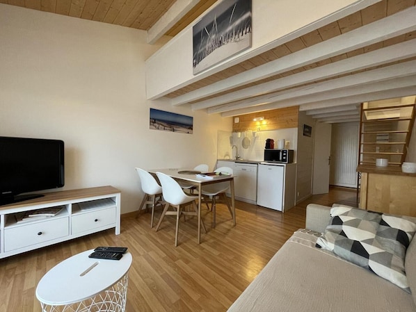 Un espacio habitable compacto con televisión, comedor, kitchenette y sofá.