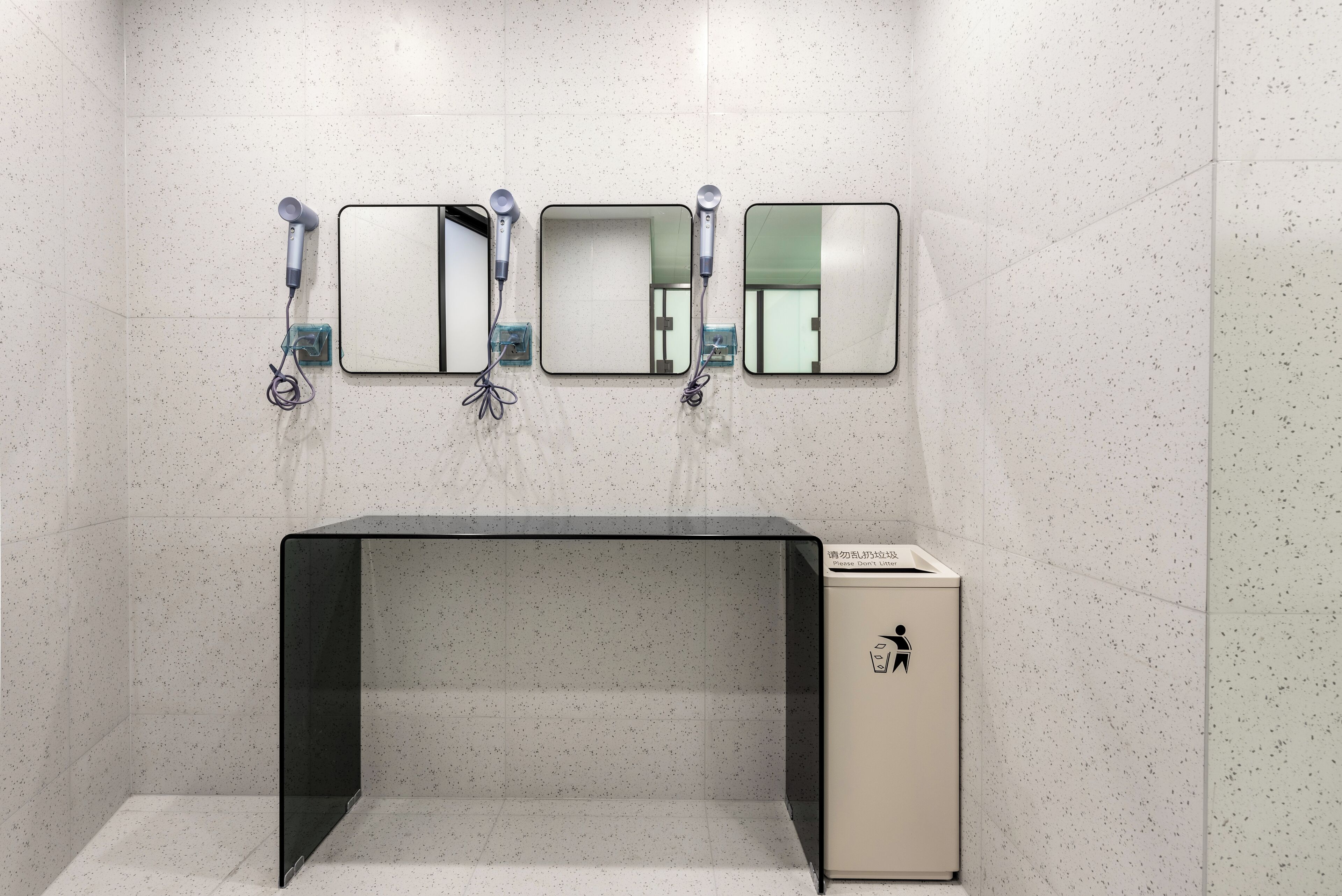 A restroom with three mirrors, a black bench, and a trash bin.