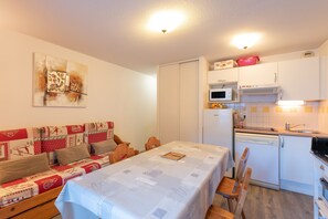 Un espace de vie compact comprenant une table à manger, un canapé avec un couvre-lit, un coin cuisine avec un four à micro-ondes et un lave-vaisselle, ainsi qu’un luminaire au plafond.