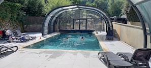 A swimming pool with a glass enclosure, lounge chairs, and a stone wall. - Comfortable Stay in Saint-Lary – 3 Apartment, Terrace, Heated Pool, and Direct Cable Car Access (Saint-Lary-Soulan)