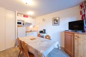 A compact kitchen with a dining table, chairs, a microwave, a refrigerator, and a television on a wooden cabinet. - Comfortable Stay in Saint-Lary – 3 Apartment, Terrace, Heated Pool, and Direct Cable Car Access (Saint-Lary-Soulan)