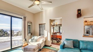 A spacious living room with a large window, a ceiling fan, and a view of the outdoors. - 4 Mi to Black Canyon: Mtn-View Apt in Montrose! (Montrose)
