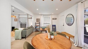 Ein modernes Wohnzimmer mit einem runden Holzesstisch, grünen Sofas und einem großen Fenster mit Vorhängen.